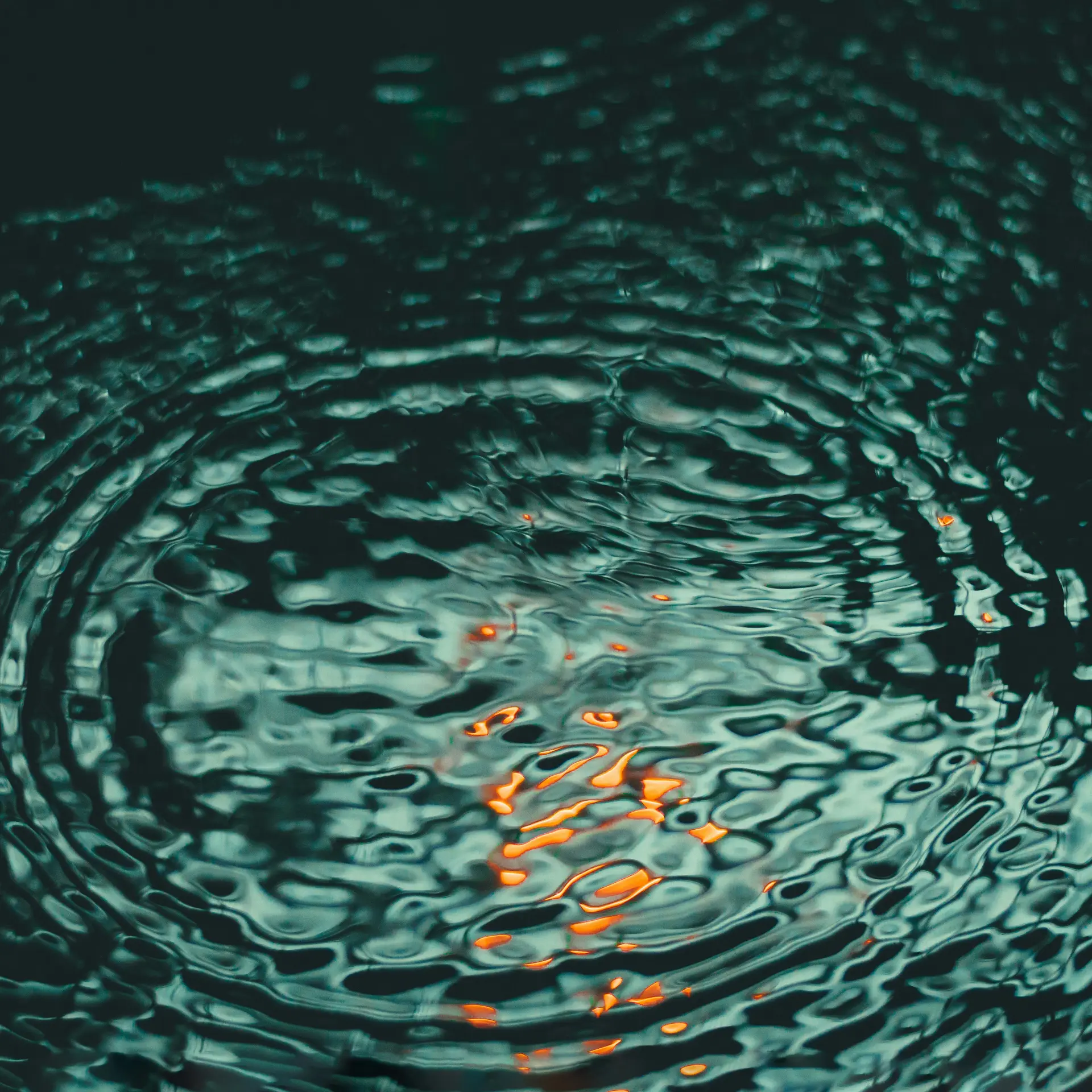 Wasseroberfläche mit konzentrischen Wellen und orangefarbenen Lichtreflexen