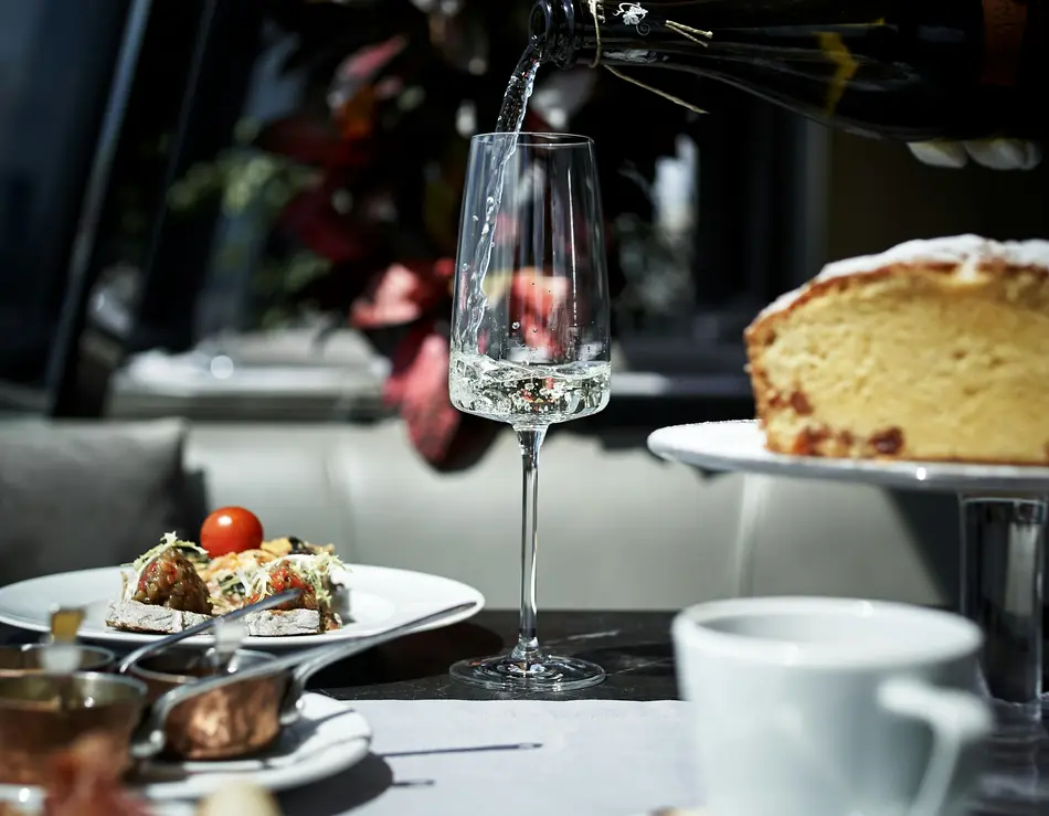 Urlaub an der Großglockner Hochalpenstraße mit Frühstück im glockna Sekt wird in ein Glas eingeschenkt, umgeben von Kuchen und Snacks auf dem Tisch