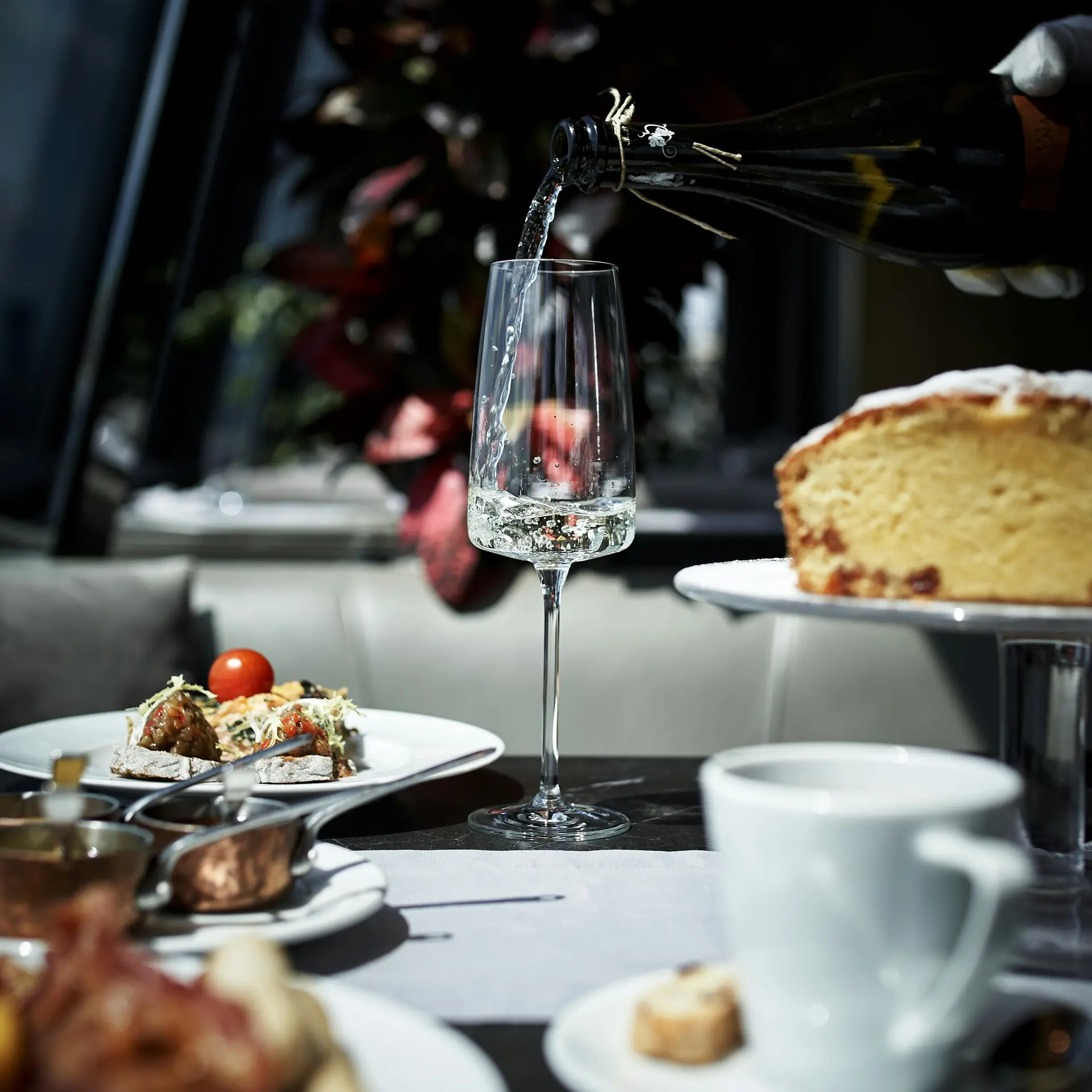 Sekt wird in ein Glas eingeschenkt, umgeben von Kuchen und Snacks auf dem Tisch