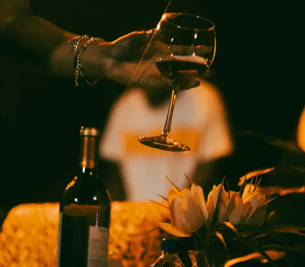 Events on the Grossglockner High Alpine Road Hand holding a wine glass above a table with wine bottle and flowers at night