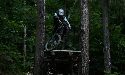 Mountainbiker springt mit Helm und Schutzkleidung zwischen Bäumen im Wald