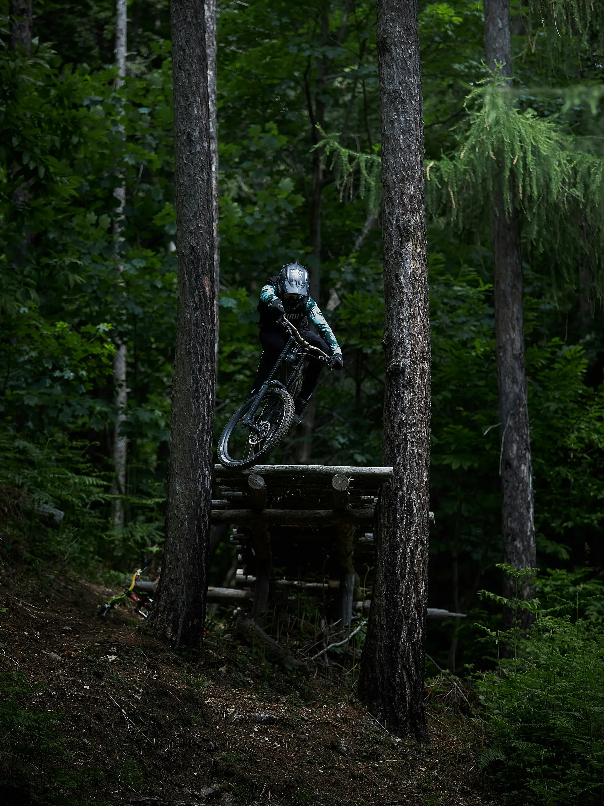 Mountainbiker springt mit Helm und Schutzkleidung zwischen Bäumen im Wald