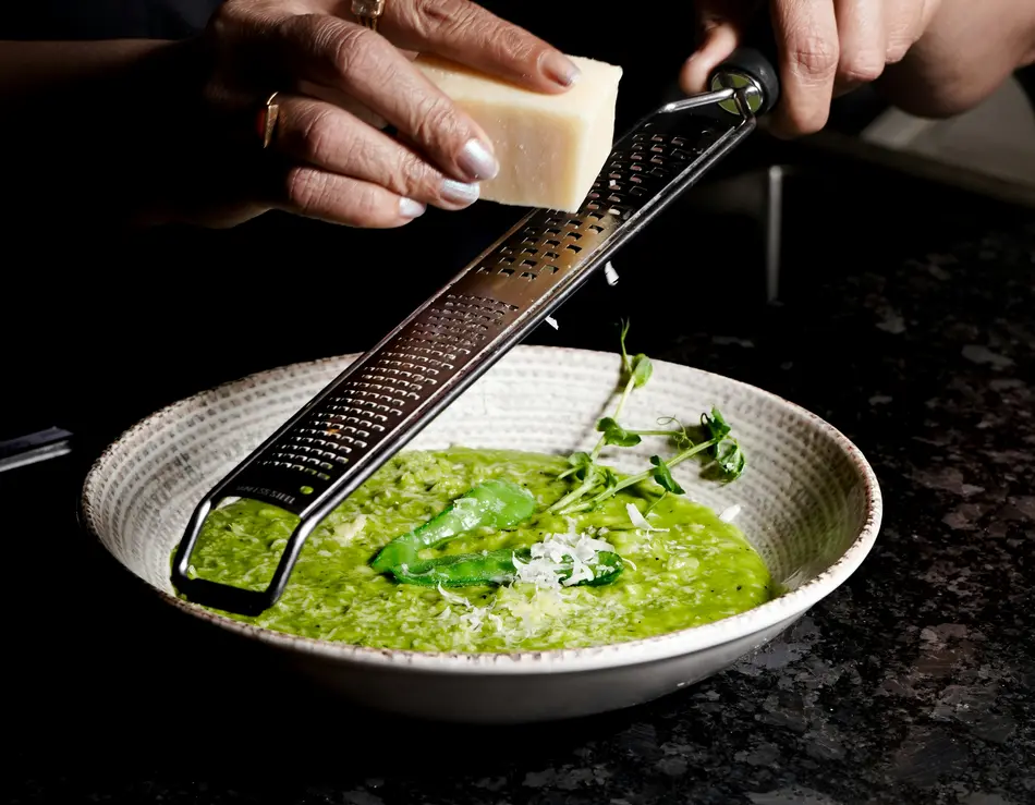 Beste Kulinarik im Hotel in Österreich: direkt in Fusch Person reibt Käse über grünes Risotto in weißem Teller