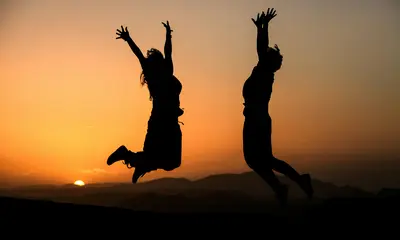 Silhouetten von zwei springenden Personen vor einem Sonnenuntergang