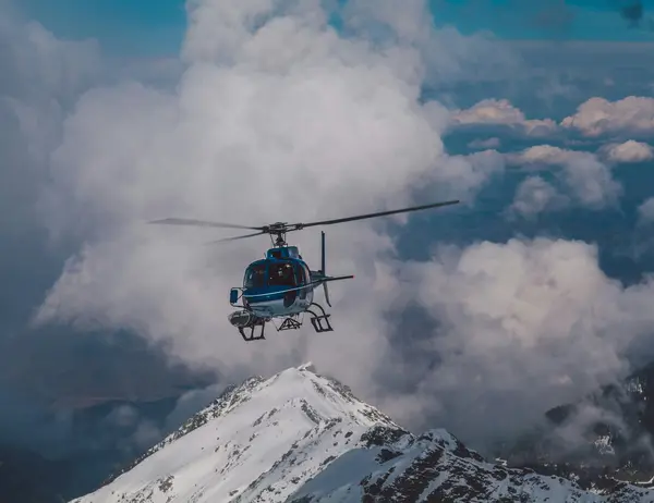 Der Aktivurlaub im SalzburgerLand mit Beschleuniger Hubschrauber fliegt über schneebedeckten Berg vor wolkigem Himmel