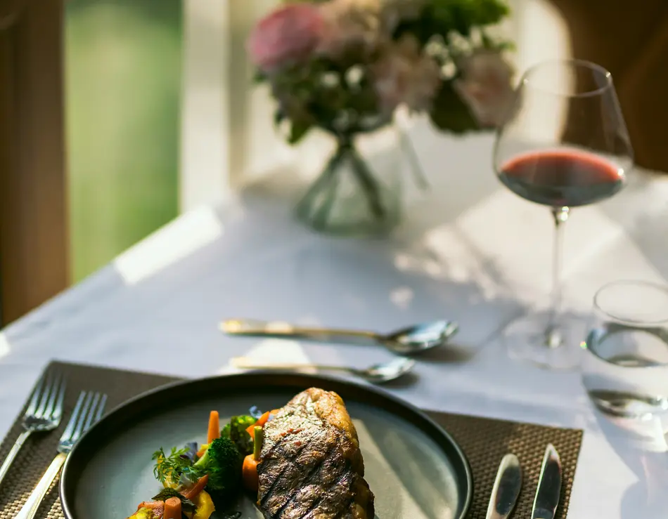 Restaurant in Fusch an der Großglocknerstraße gesucht? Gegrilltes Steak mit Gemüse auf schwarzem Teller neben Glas Rotwein auf gedecktem Tisch