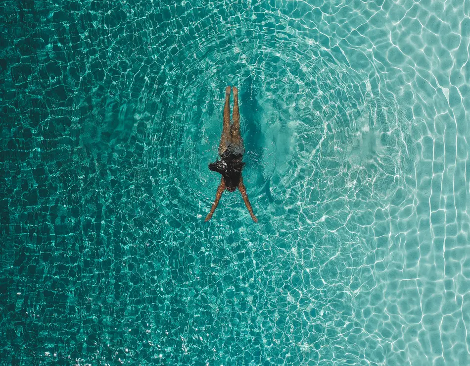 Der schönste Infinitypool im SalzburgerLand – im glockna Frau schwimmt auf dem Rücken in klarem blauem Wasser von oben gesehen