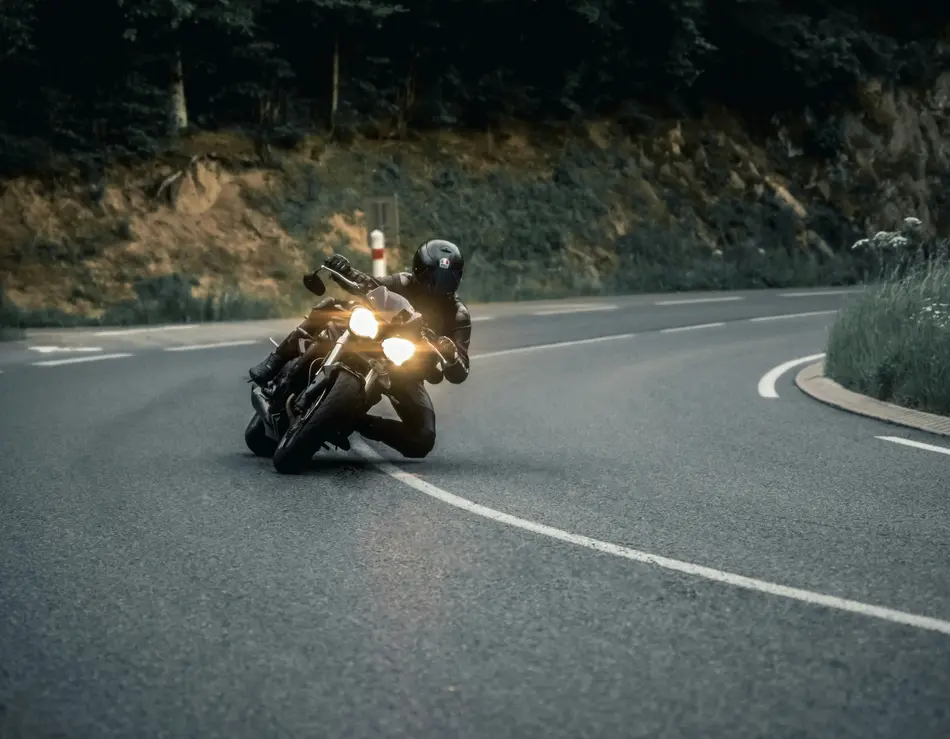 Dein Motorradhotel an der Großglockner Hochalpenstraße Motorradfahrer fährt in Kurve auf bergiger Straße mit Wald im Hintergrund