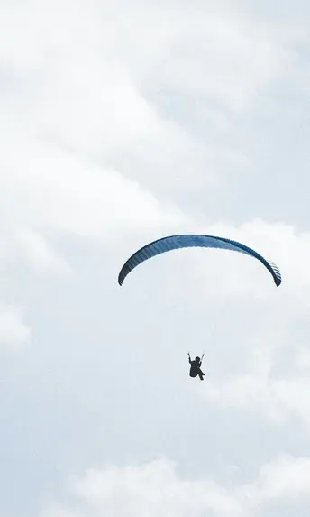 Person beim Gleitschirmfliegen vor bewölktem Himmel