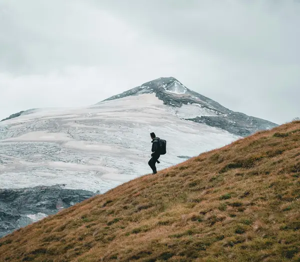 Sehenswürdigkeiten in Fusch und Umgebung Wanderer geht auf grasigem Hang mit schneebedecktem Berg im Hintergrund unter bewölktem Himmel