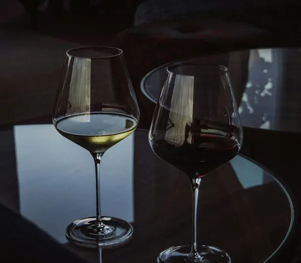 Beste Kulinarik im Hotel in Österreich: direkt in Fusch Zwei Weingläser mit rotem und weißem Wein auf einem Glastisch in dunklem Raum