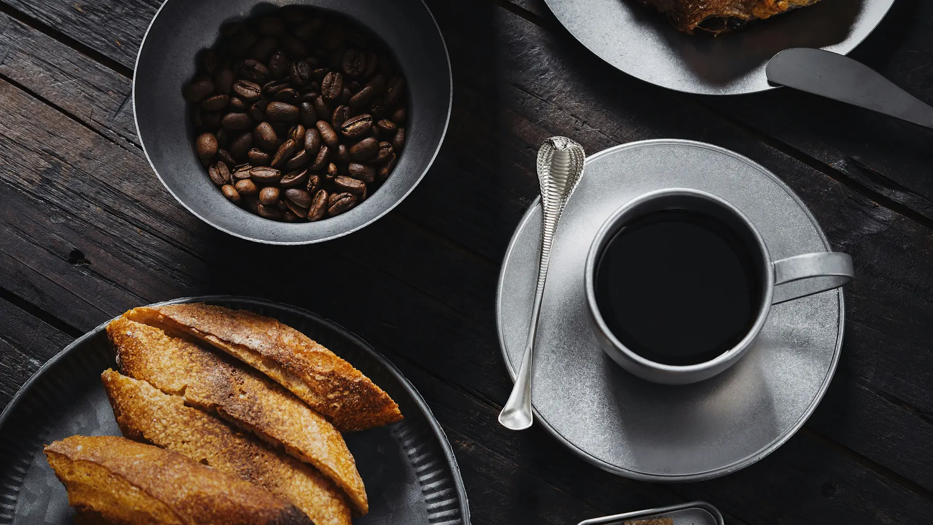 Urlaub an der Großglockner Hochalpenstraße mit Frühstück im glockna Tasse schwarzer Kaffee, Kaffeebohnen und Gebäck auf dunklem Holztisch