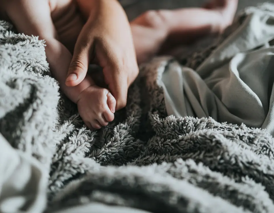 Dein Familienurlaub im SalzburgerLand Erwachsene Hand hält Babyhand auf weicher grauer Decke