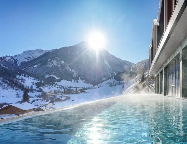 Infinity-Pool mit Bergblick und Sonnenschein in verschneiter Winterlandschaft