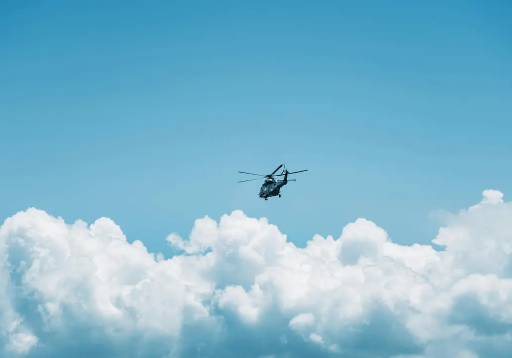 Hubschrauber fliegt über weiße Wolken vor blauem Himmel