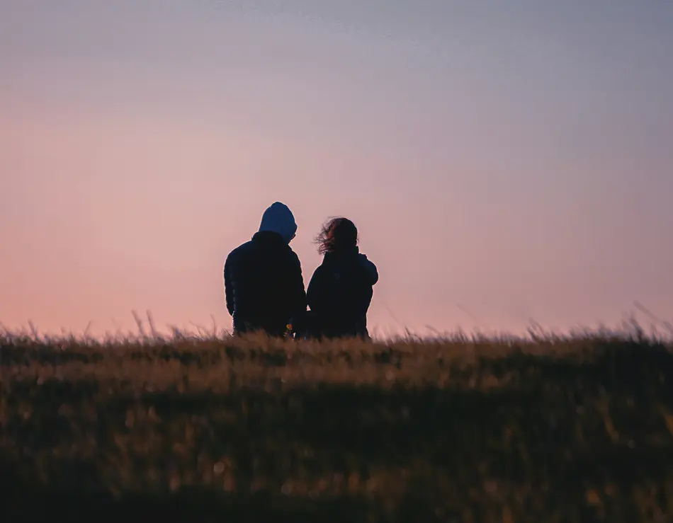 The team behind glockna – owner-run with passion Two people sitting in a field at sunset