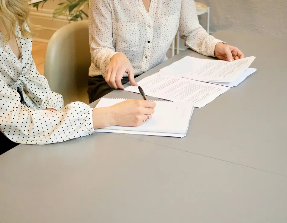 Stellenangebote für Fusch Zwei Frauen in gepunkteten Blusen arbeiten an Dokumenten an einem grauen Tisch
