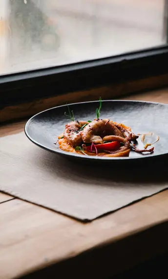 Restaurant in Fusch an der Großglocknerstraße gesucht? Gourmetgericht mit gebratenem Tintenfisch und Gemüse auf schwarzem Teller