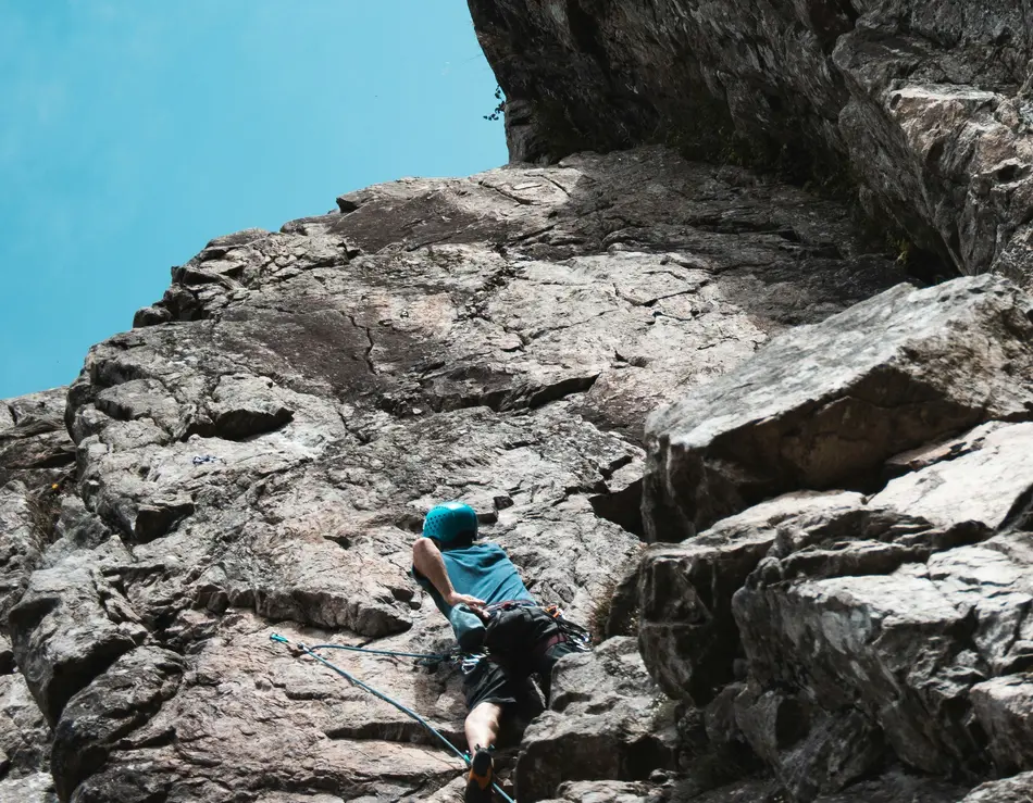 Bergsteigen mit Blick auf den Großglockner Kletterer in blauer Kleidung erklimmt steilen Felsen unter blauem Himmel