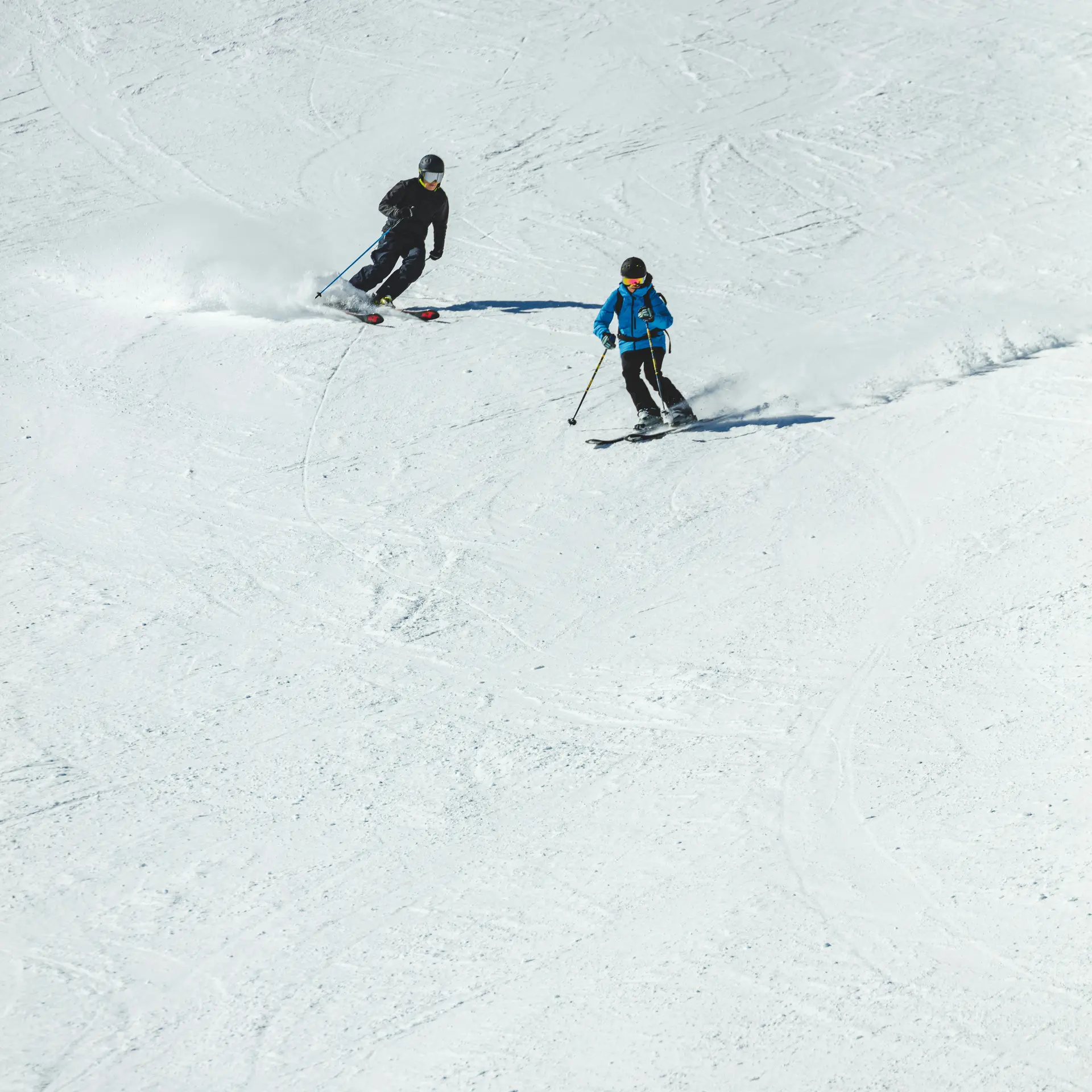 Zwei Skifahrer fahren nebeneinander auf einer verschneiten Piste