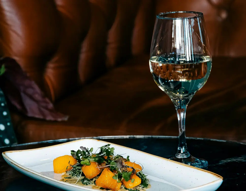 Events on the Grossglockner High Alpine Road Glass of white wine and plate with pumpkin and microgreens on black table