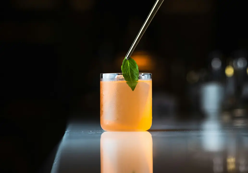 Beste Kulinarik im Hotel in Österreich: direkt in Fusch Hand legt mit einer Zange ein grünes Blatt als Garnitur auf einen orangen Cocktail
