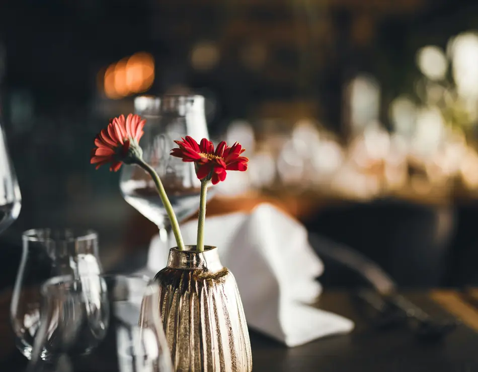 Beste Kulinarik im Hotel in Österreich: direkt in Fusch Goldene Vase mit roten Blumen auf einem gedeckten Restauranttisch