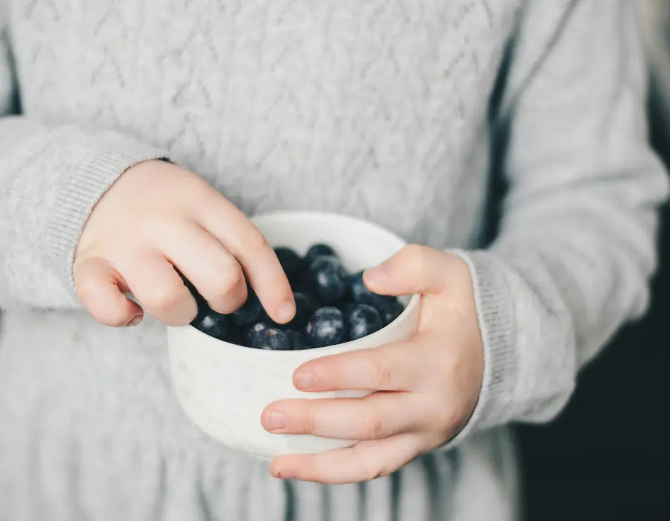 Dein Familienurlaub im SalzburgerLand Kind hält weiße Schale mit Blaubeeren und nimmt eine Beere heraus