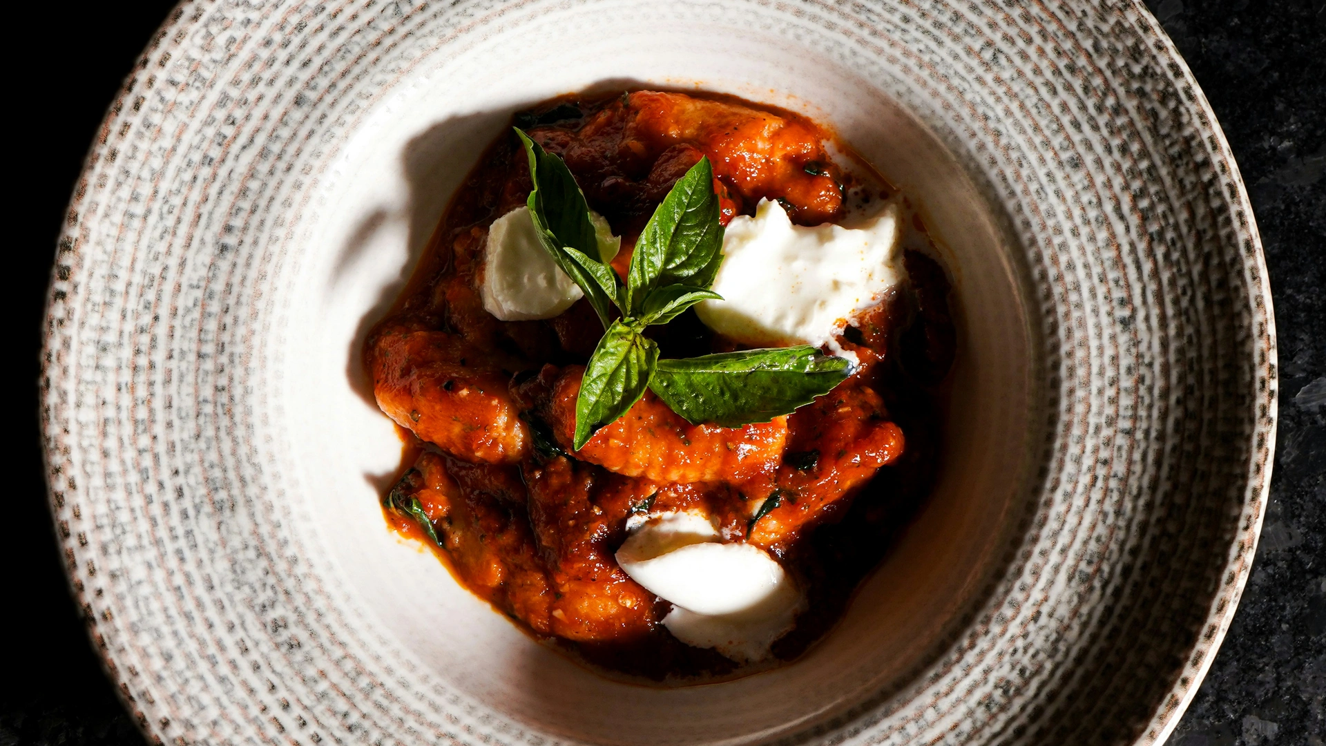 Gnocchi mit Tomatensauce, Mozzarella und Basilikum in einem gemusterten Teller