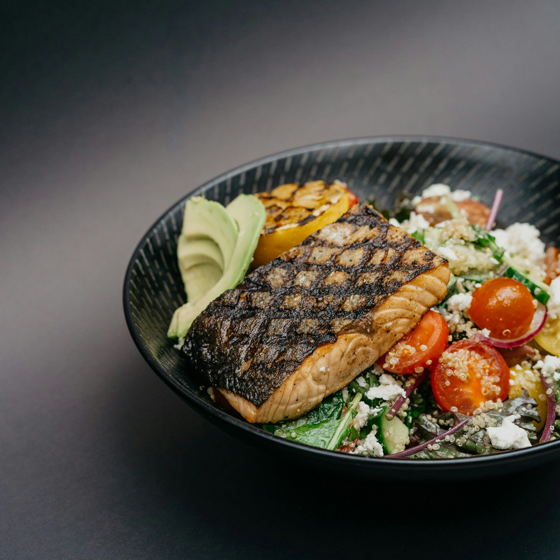 Gegrilltes Lachsfilet mit Avocado, gegrillter Zitrone und gemischtem Salat im schwarzen Teller