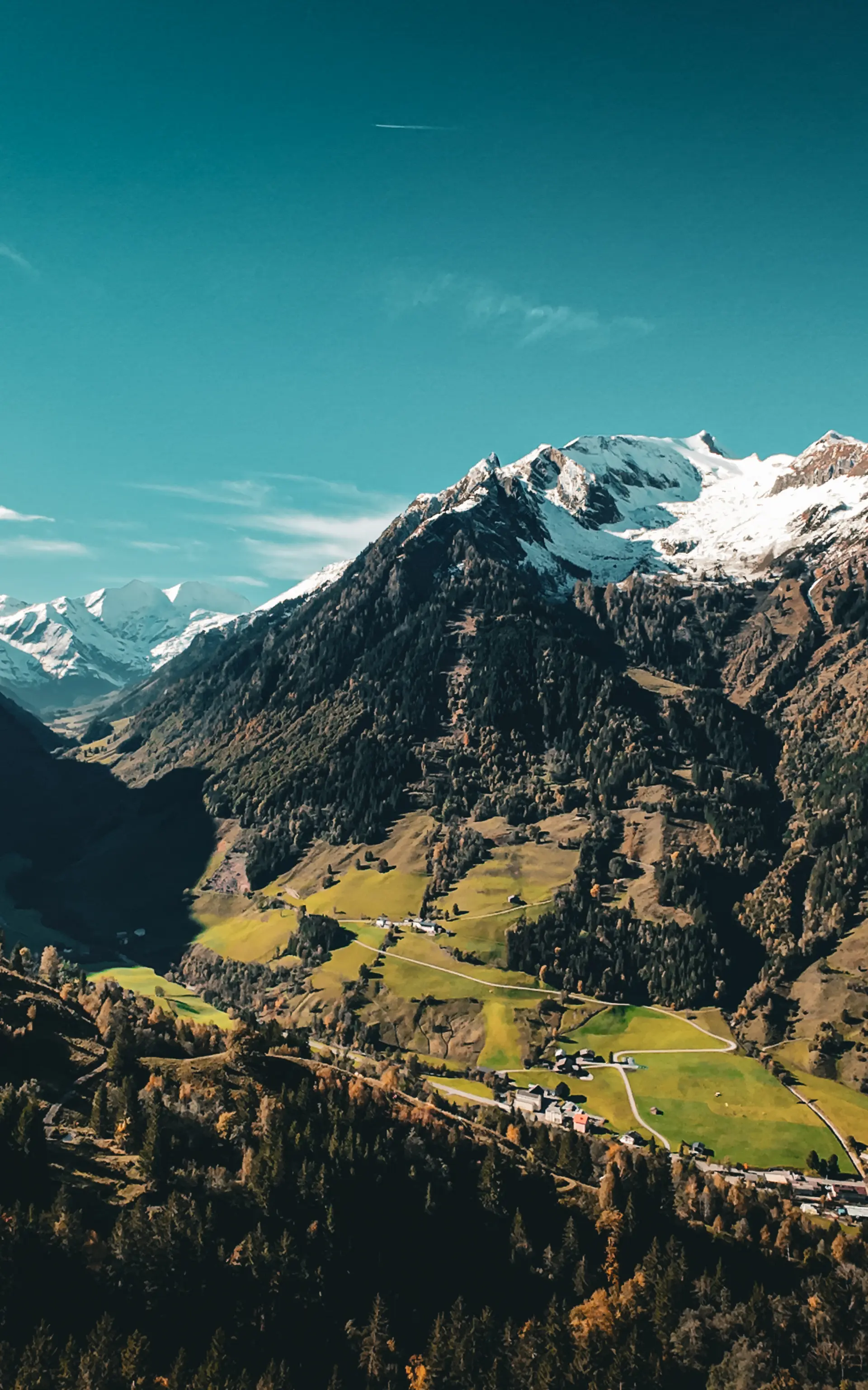 Bergtal mit schneebedeckten Gipfeln und grünen Wiesen unter blauem Himmel