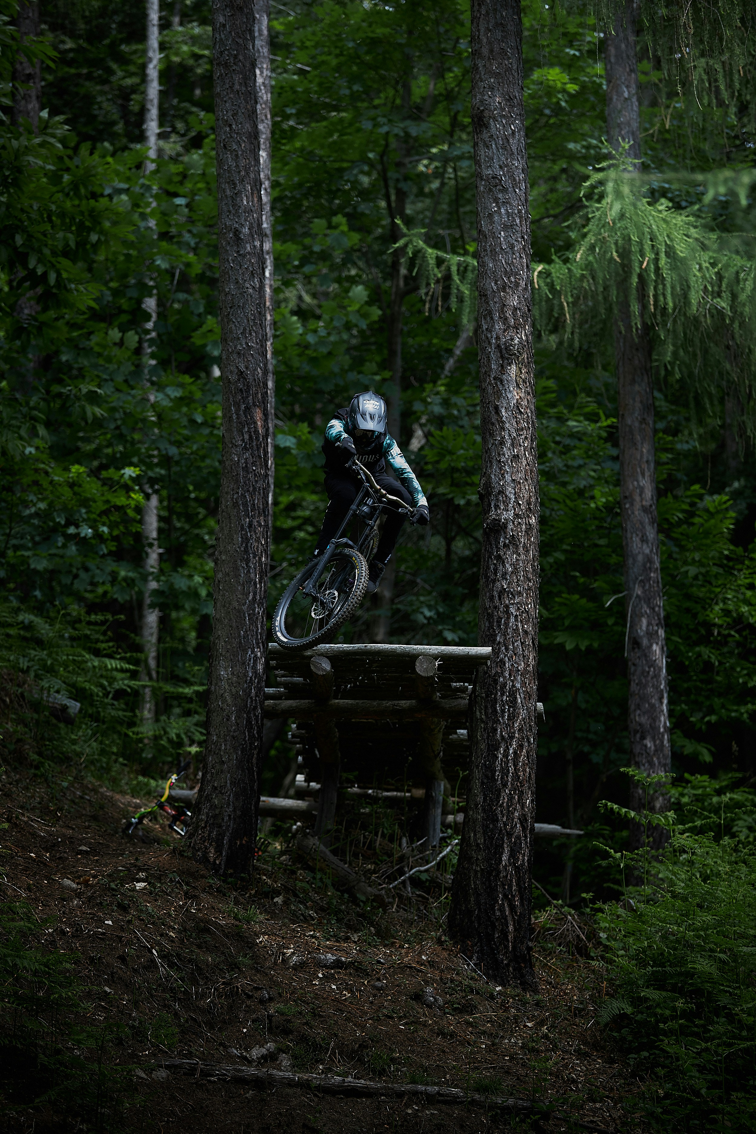 Mountainbiker springt mit Helm und Schutzkleidung zwischen Bäumen im Wald