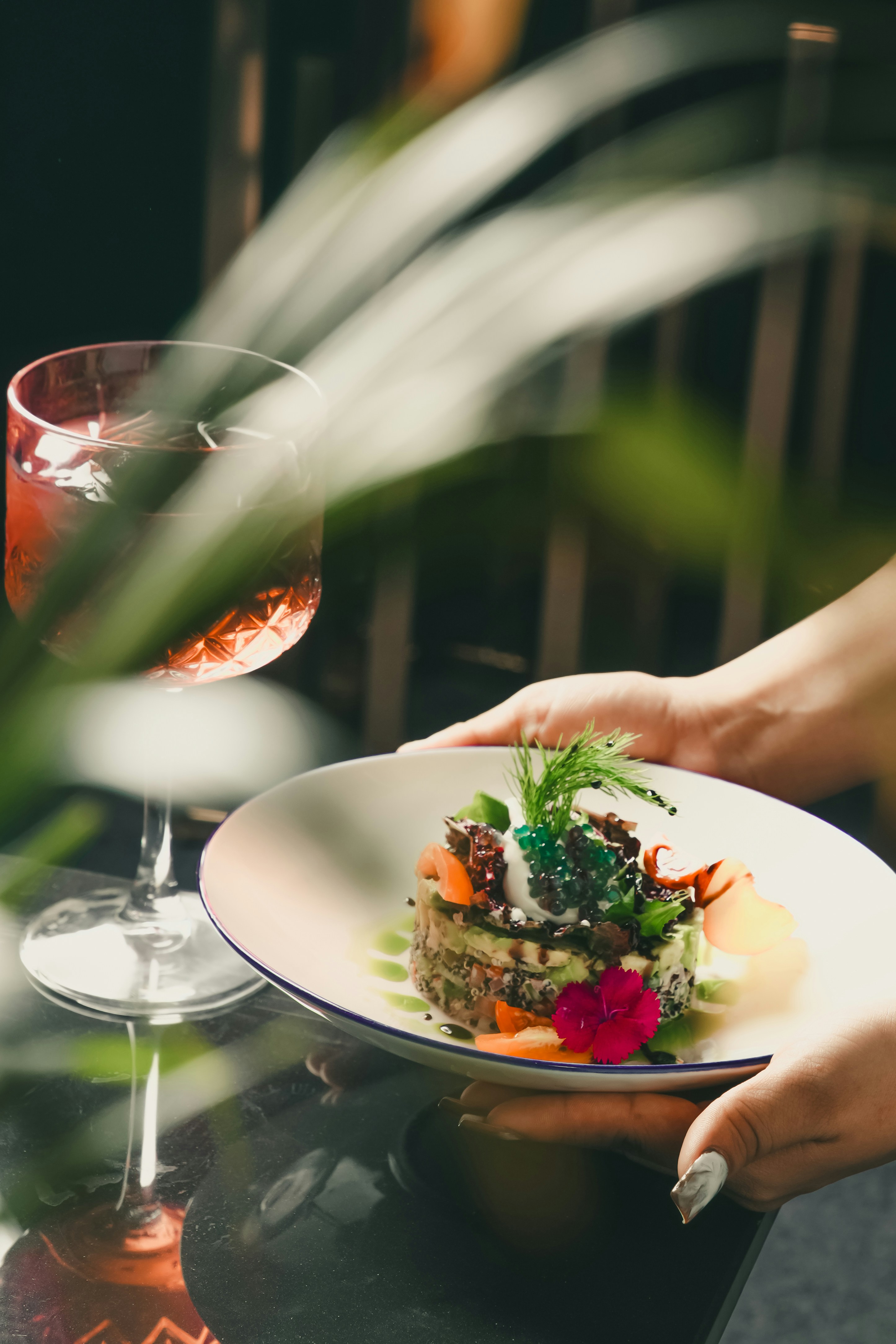 glockna, your gourmet hotel in the Salzburg region Hands holding plate with artfully arranged gourmet dish next to a glass of drink