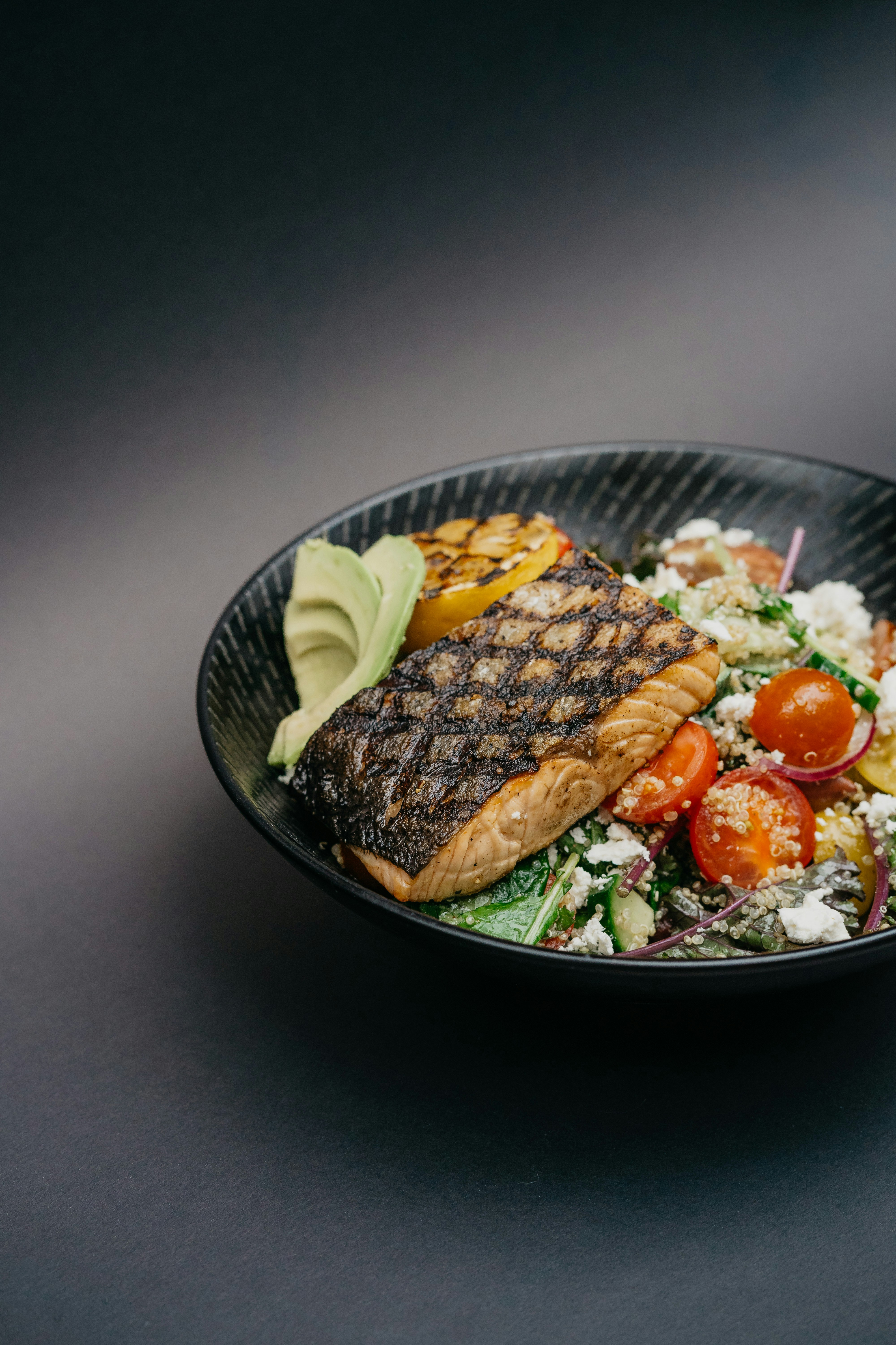 Gegrilltes Lachsfilet mit Avocado, gegrillter Zitrone und gemischtem Salat im schwarzen Teller