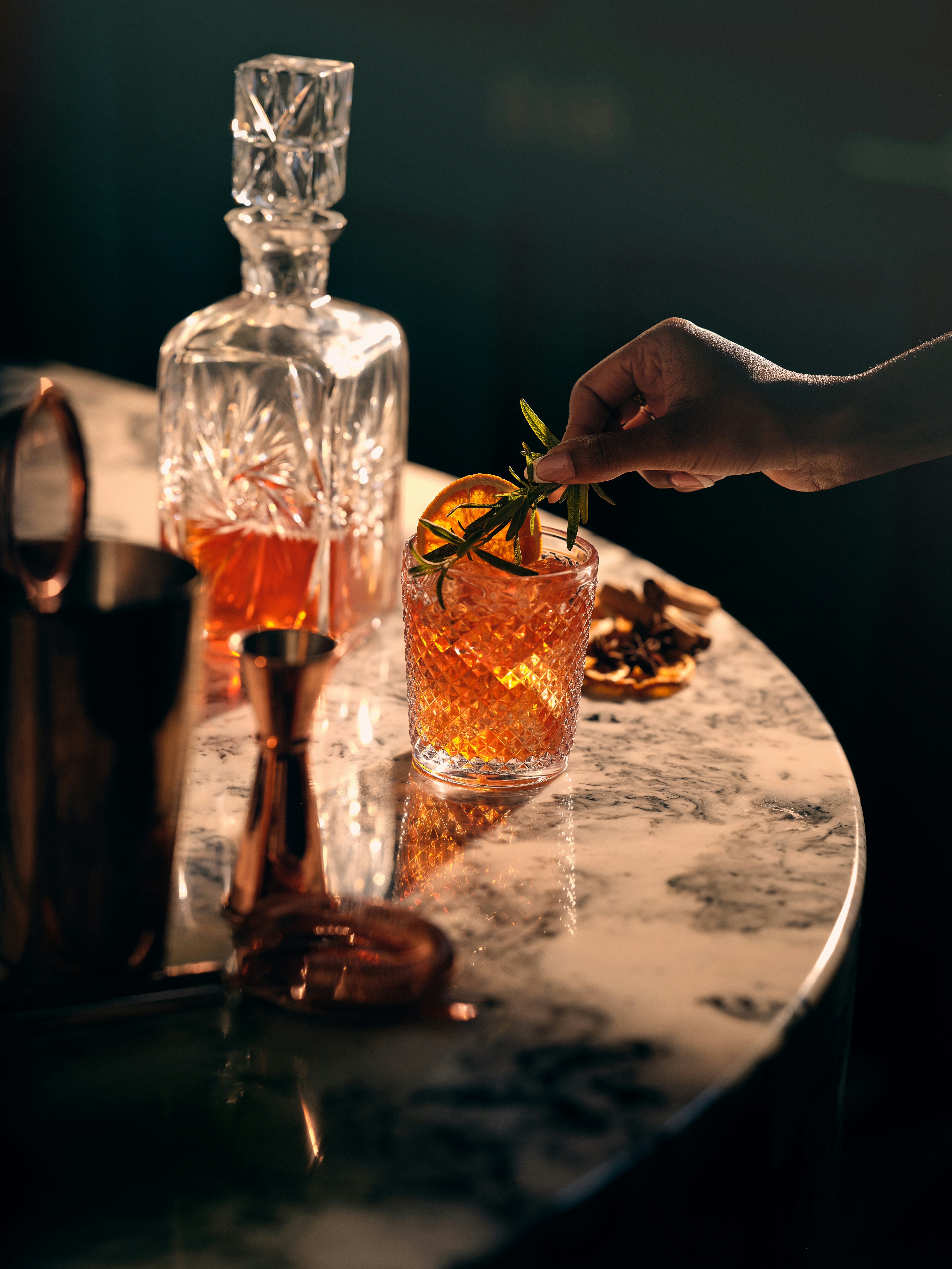 Events on the Grossglockner High Alpine Road Hand garnishing cocktail with orange slice and herbs on marble surface