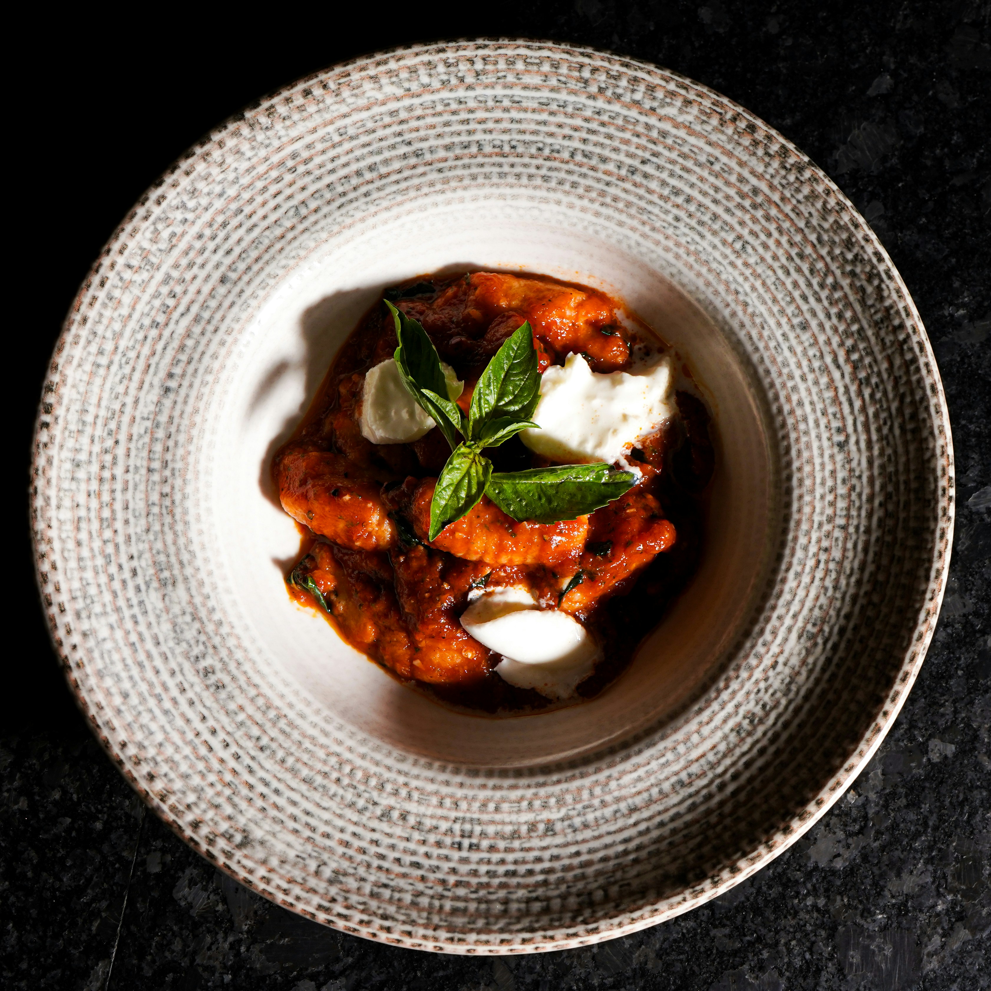 Gnocchi mit Tomatensauce, Mozzarella und Basilikum in einem gemusterten Teller