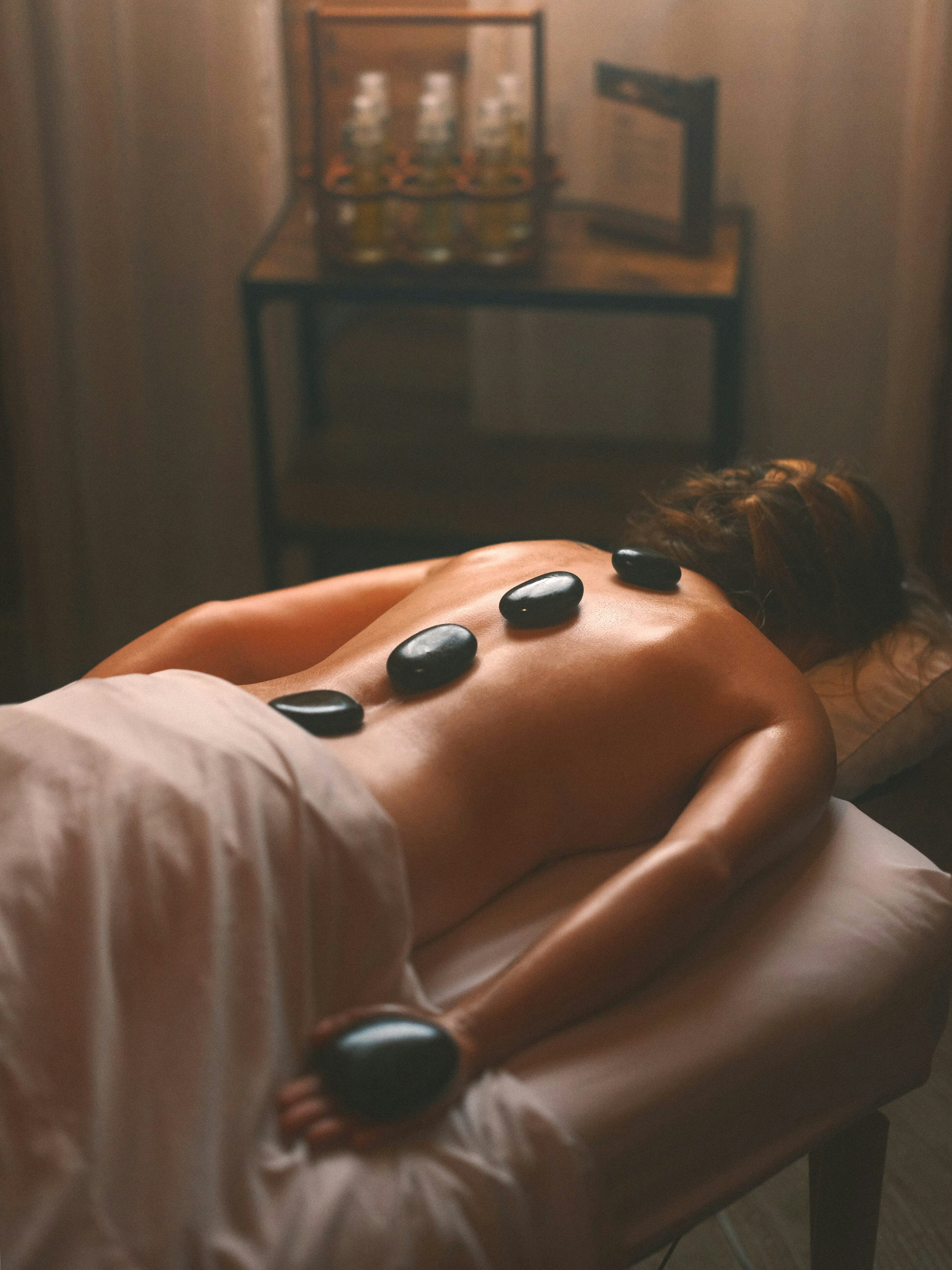 Person liegt auf Massagetisch mit heißen Steinen auf dem Rücken
